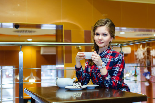 Young nice girl in a plaid shirt drinking tea in a cafe