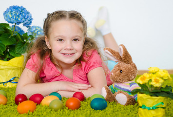 Fototapeta na wymiar Smiling little girl lying with Easter eggs on green carpet
