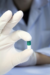 Close-up hand in medical rubber glove holding one green and whit