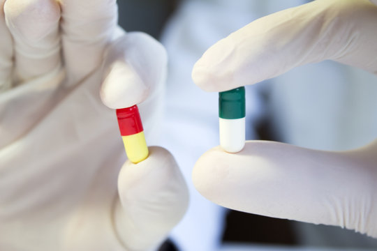 Hands in medical gloves holding different capsules