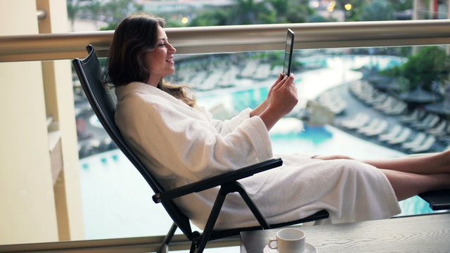 Pretty woman in bathrobe chatting on tablet computer sitting 
