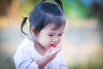 Cute little girl is eating mulberry with sour feeling