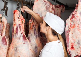Female Butcher Hanging Meat In Butchery
