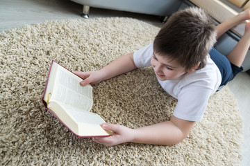 Boy reading a book while lying on  carpet in the room