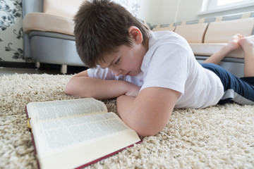 Boy reading a book while lying on  carpet in the room