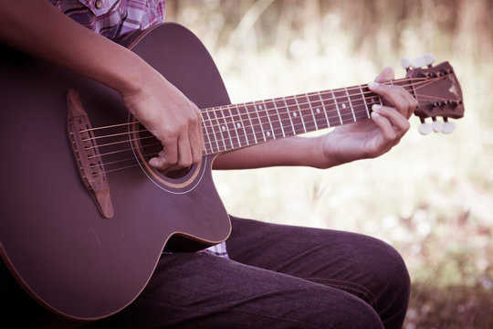 Male hand playing acoustic guitar on meadow background in retro