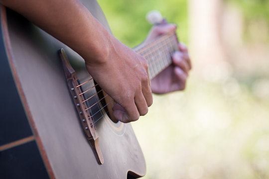 Male hand playing acoustic guitar on meadow background