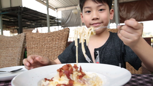Little asian child eating pasta at restaurant .