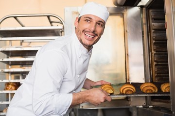 Happy baker taking out fresh croissants