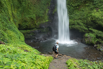 Obraz premium Man standing by lush green Jungle waterfall in Indonesia