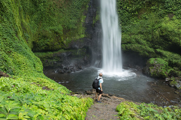 Man standing by lush green Jungle waterfall in Indonesia