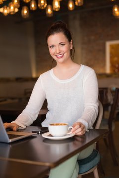 Pretty brunette having coffee using laptop