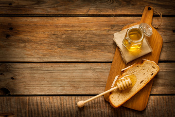 Honey in a jar, slice of bread and honey dipper on vintage wood