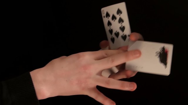Hands of magician doing a magic trick with cards on black