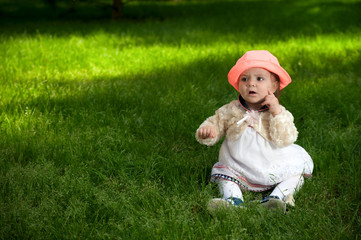 A little baby in bright hat is sitting on the grass