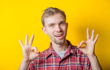 Portrait of funny man showing OK gesture with hands against yellow background