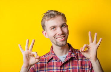 Portrait of funny man showing OK gesture with hands against yellow background