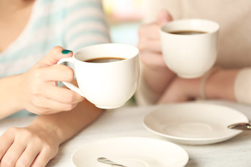 Fototapeta na wymiar Two women with cups of coffee on bright background