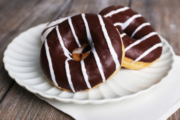 Delicious donuts with icing on plate on wooden background