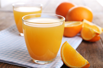 Glasses of orange juice with oranges on wooden table close up