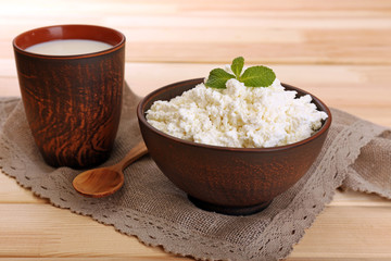 Cottage cheese in bowl with cup of milk on wooden background