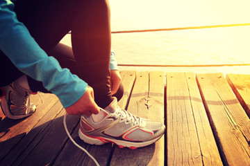 young woman runner tying shoelaces on sunrise seaside boardwalk