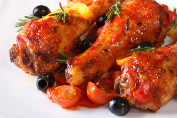 Fried chicken legs in tomato sauce with peppers on a plate macro