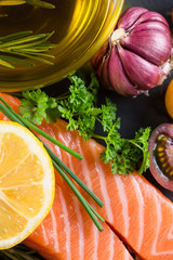 Portion of fresh salmon and herbs on black background