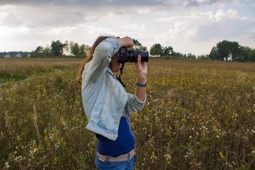 Fototapeta premium Девушка фотографирует в поле