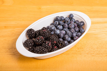 Black and Blue Berries in White Bowl on Wood Table
