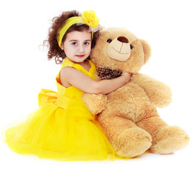 Fashionable dark-haired little girl hugging a bear
