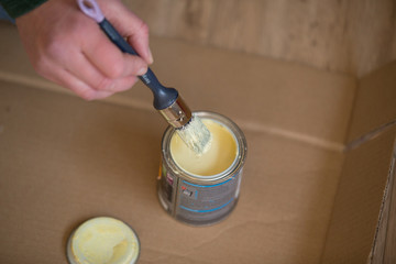 Dipping a paintbrush in a can of yellow paint