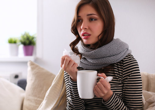 Sick woman covered with blanket holding cup of tea sitting on