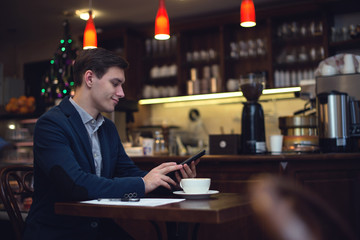 Young attractive businessman in a suit drinking coffee and using