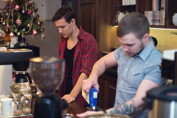 Two hipsters working in a coffee shop making orders cleaning the