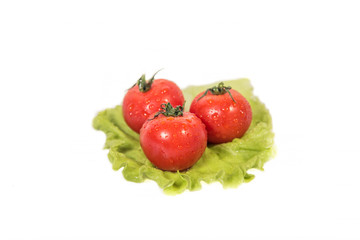 Three tomatoes lying on a sheet of green salad