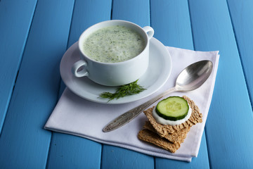 Cucumber soup in bowl on color wooden planks background