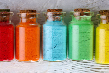 Bottles with colorful dry pigments on wooden background