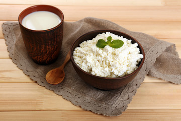 Cottage cheese in bowl with cup of milk on wooden background