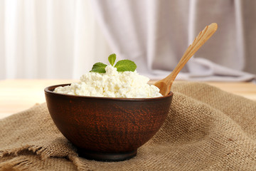 Cottage cheese in bowl with spoon on table on fabric background