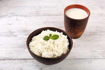 Cottage cheese in bowl with cup of milk on wooden background