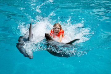 Fototapeta premium Szczęśliwa dziewczynka jedzie dwa delfiny w basenie