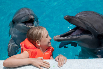 Obraz premium Szczęśliwa dziewczynka śmiejąc się z dwoma delfinami w basenie