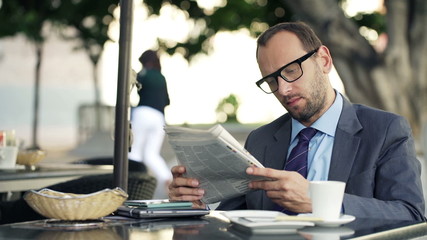 Young businessman reading newspaper sitting in cafe in city - Powered by Adobe