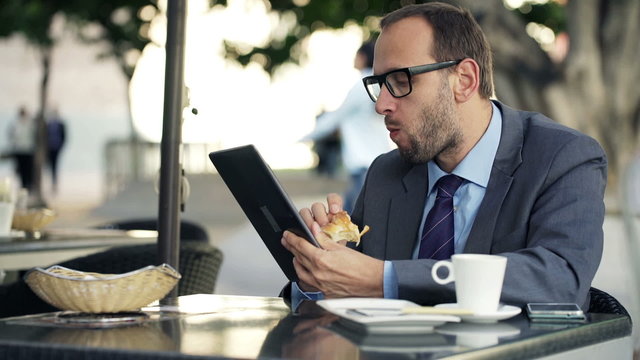 Businessman with tablet computer eating croissant in cafe