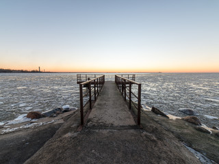 sunset over frozen sea with old metal bridge