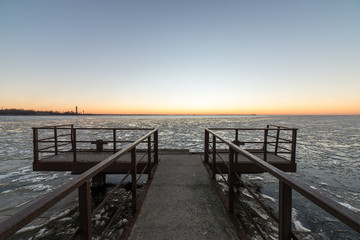 Fototapeta na wymiar sunset over frozen sea with old metal bridge
