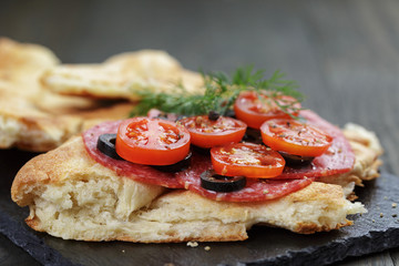 flat pita bread with salami and vegetables on wood table