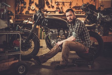 Obraz na płótnie Canvas Mechanic with cafe-racer motorcycle in custom garage