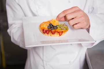Close up of baker putting flower on the pastry with fruit